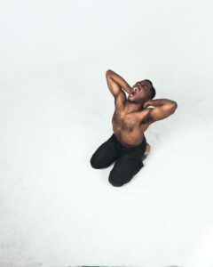 A black man crouching on the floor in front of a white background.