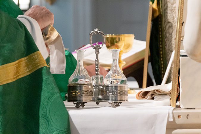 A priest in a green robe is holding a glass.