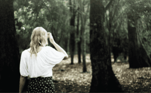 A woman in a white shirt standing in a wooded area.