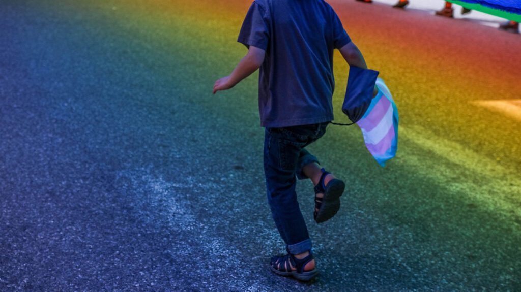 A boy running with a rainbow flag in the street.