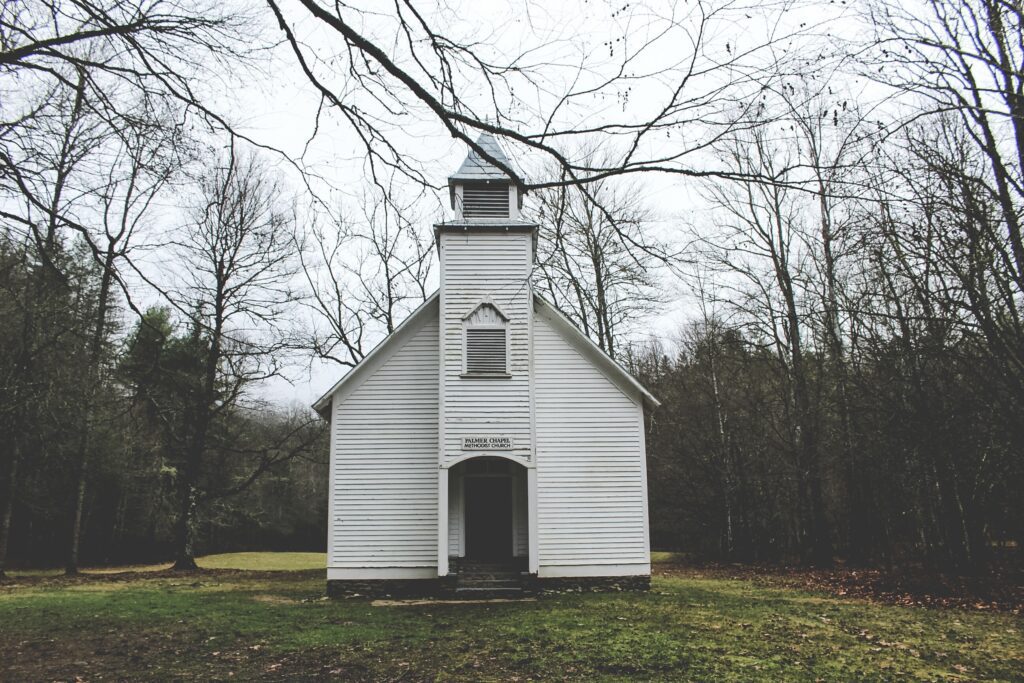 A small white church in the middle of a wooded area.