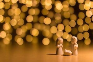 Two figurines in a nativity scene in front of a bokeh background.