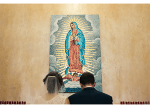 A bride and groom looking at a painting of the virgin mary.
