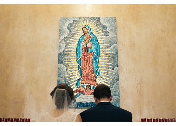 A bride and groom looking at a painting of the virgin mary.