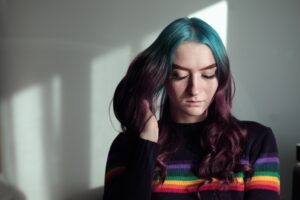 A woman with rainbow hair sitting in front of a window.