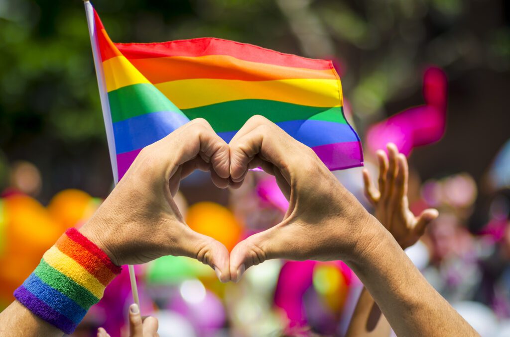 People making a heart shape with a rainbow flag.