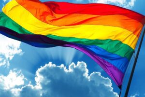 A rainbow flag waving in the wind against a blue sky.
